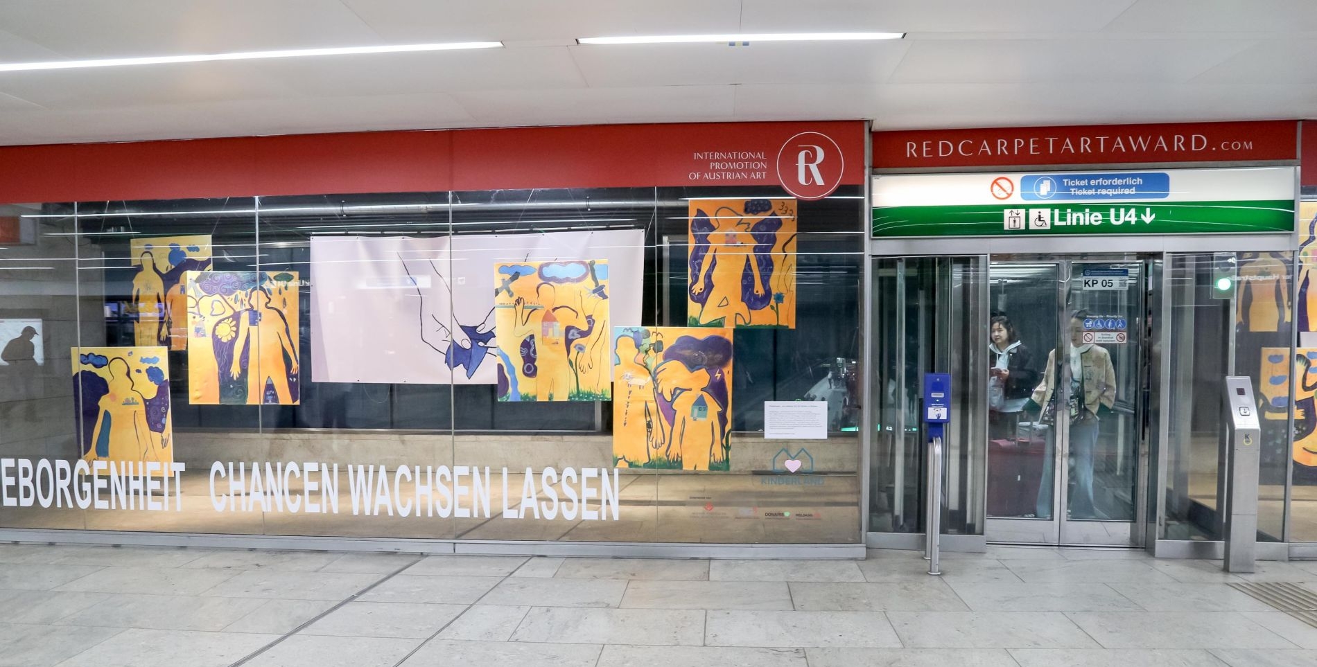 Glasfront mit einer Tür,  Links sind neben dieser Tür ausgestellt Bilder zu sehen