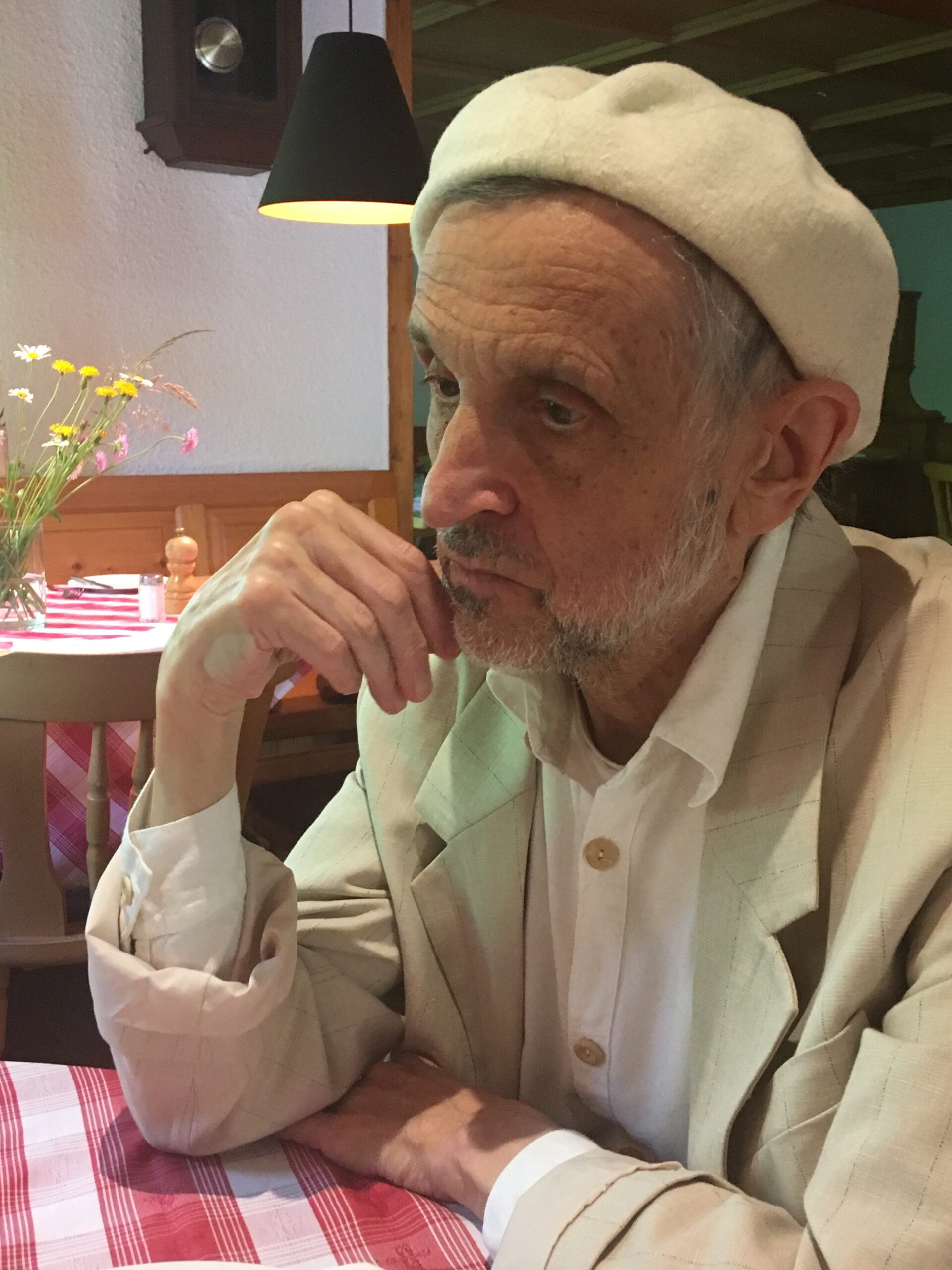 Hans-Willi Weis in nachdenklicher Pose, weiß gekleidet mit weißer Baskenmütze