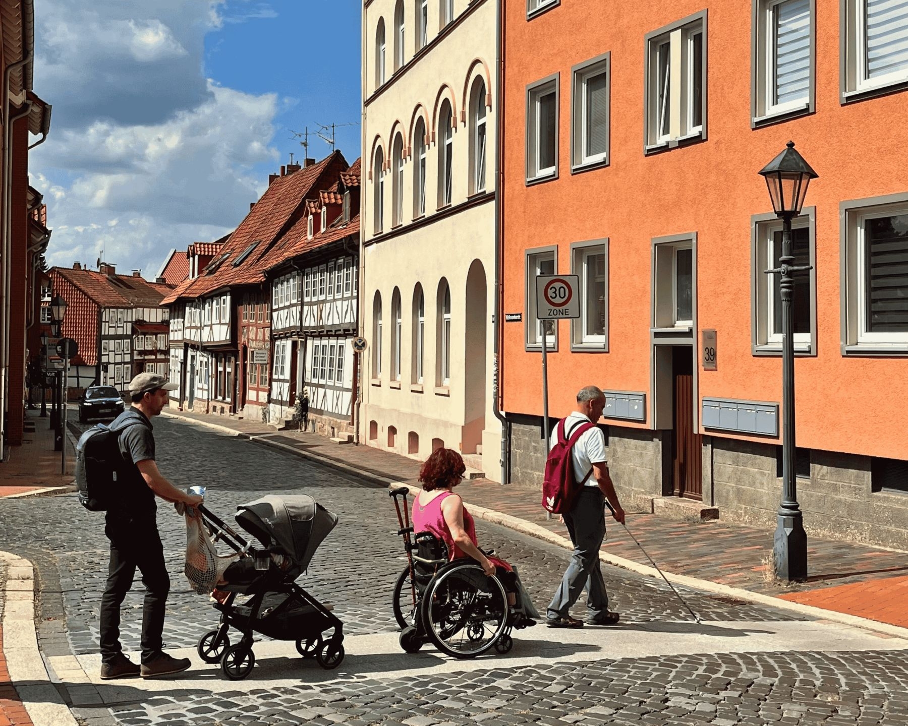 Bild zeigt eine Kopfsteinpflasterstraße, die mit einem betonierten Querweg gut barrierefrei zu überqueren ist