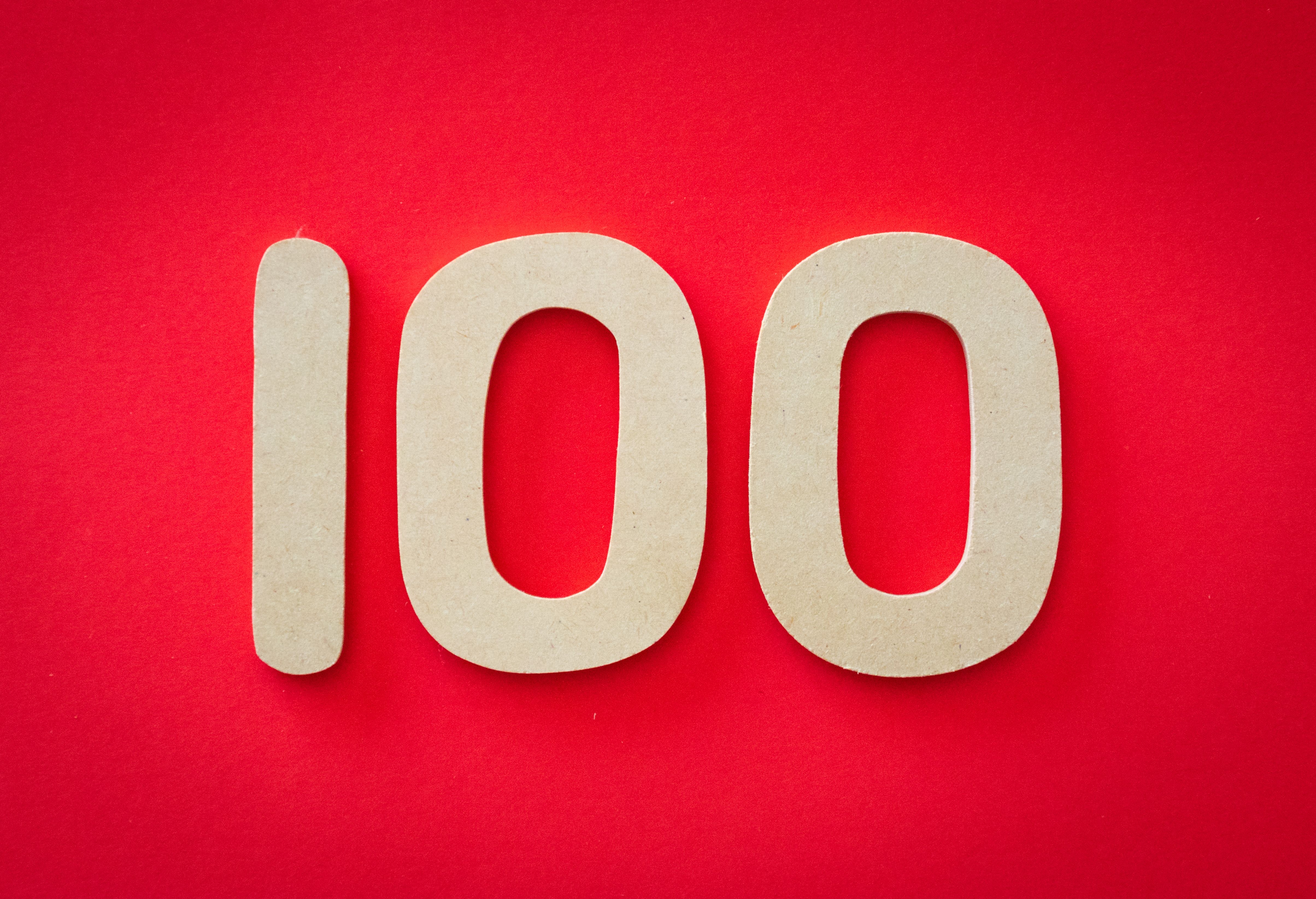 Close-up of numeral 100 in beige on a bright red background, emphasizing celebration.