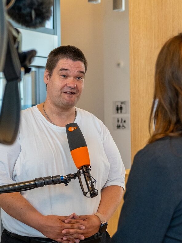 Junger Mann mit dunklem Haar und weißem Shirt vor dem Mikrofon des zdf