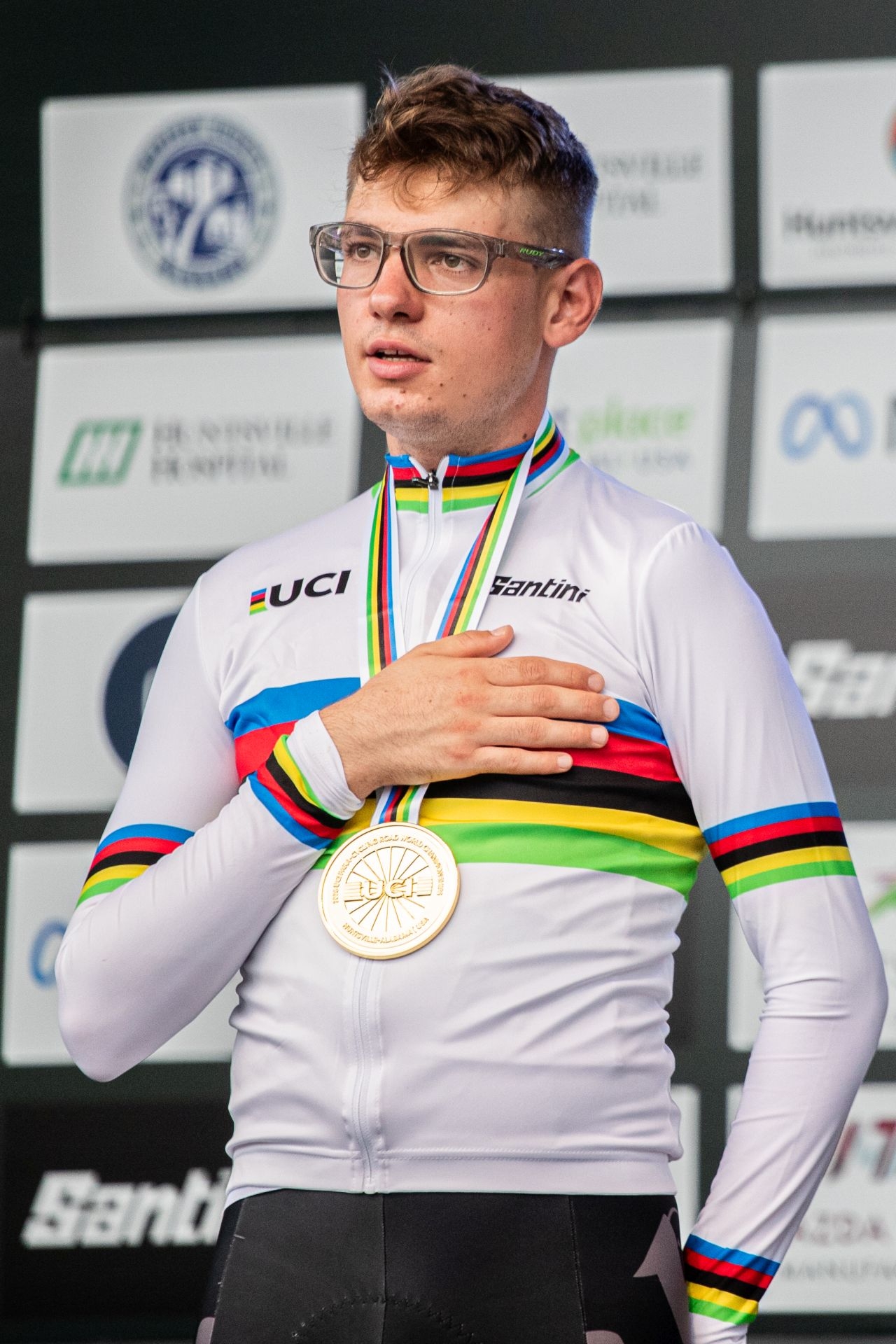 Junger Mann mit dunklem Haar und Brille in weißem T-Shirt mit umgehängter Goldmedaille