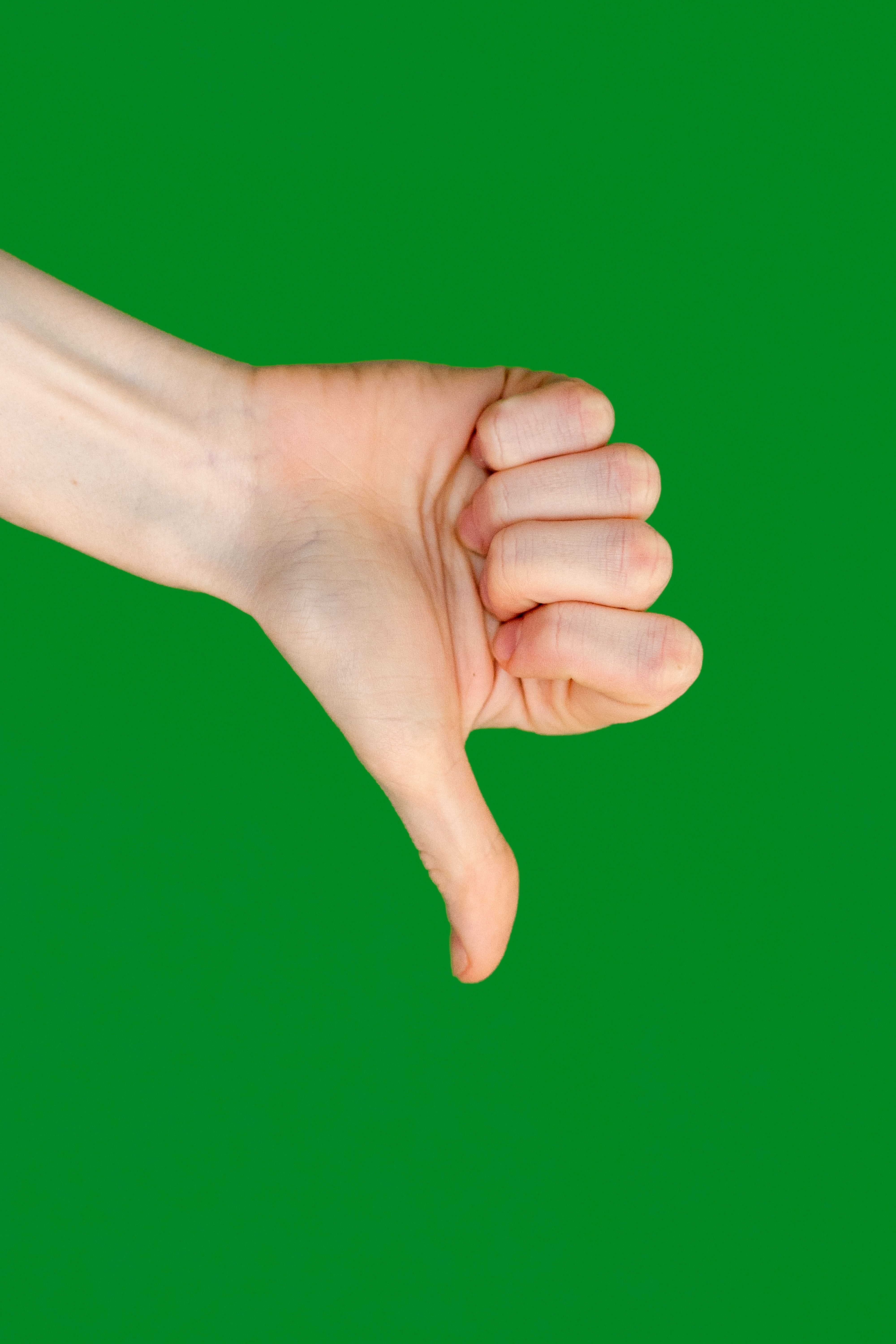 A hand displaying a thumbs down gesture against a vivid green background.