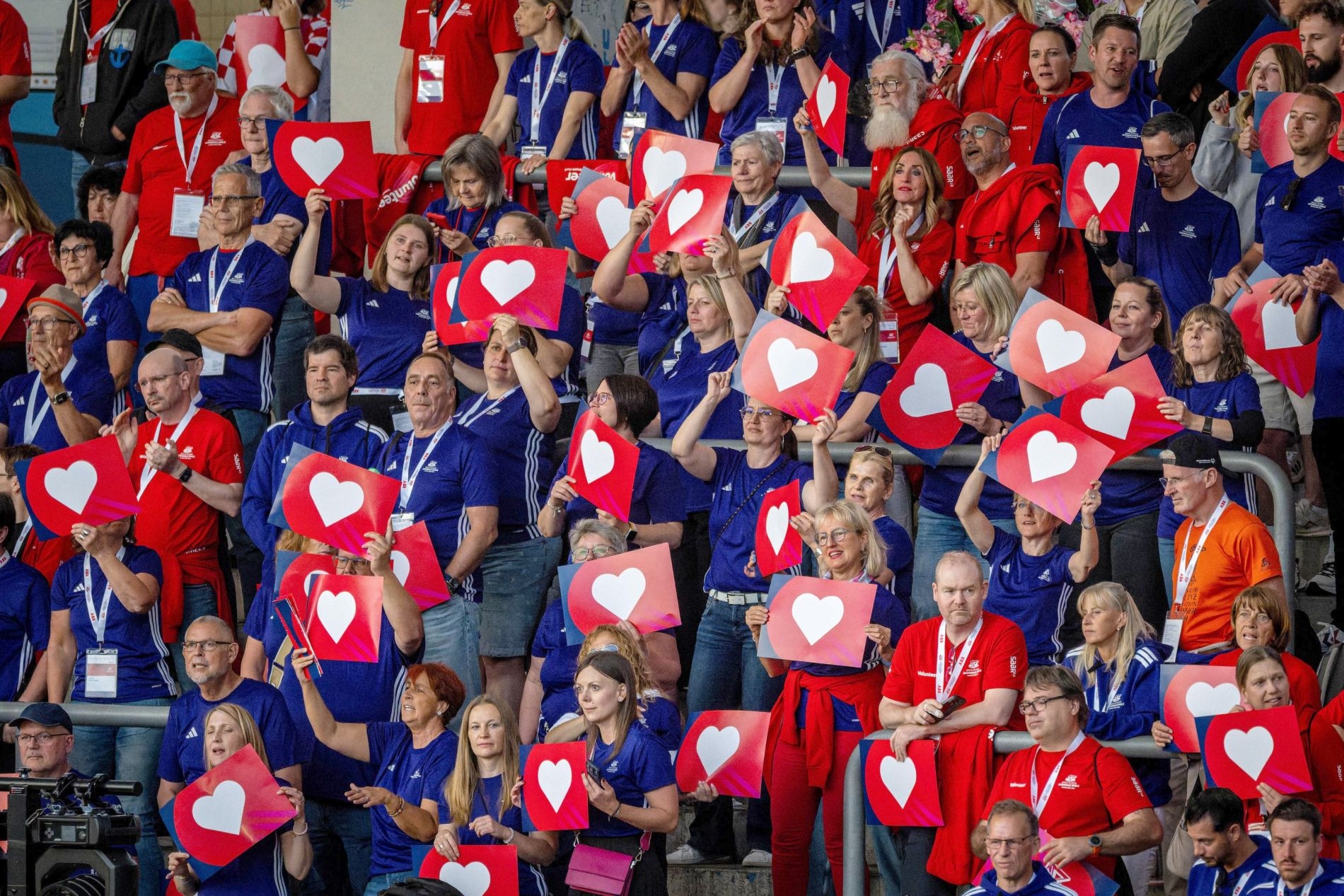 Ein Foto voller in blauem Sportdress gekleideter Menschen, die rote Tafeln mit einem weißem Herzen hochhalten