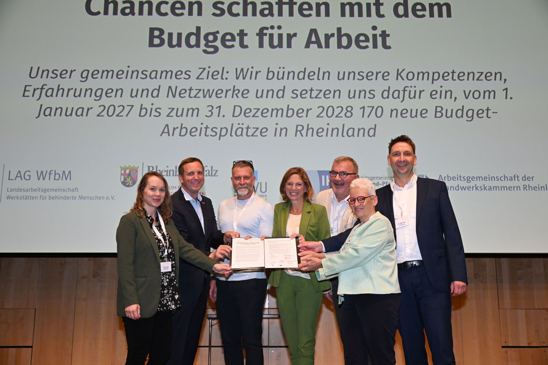 Sieben Personen stehen auf einer Bühne mit der Absichtserklärung in der Hand