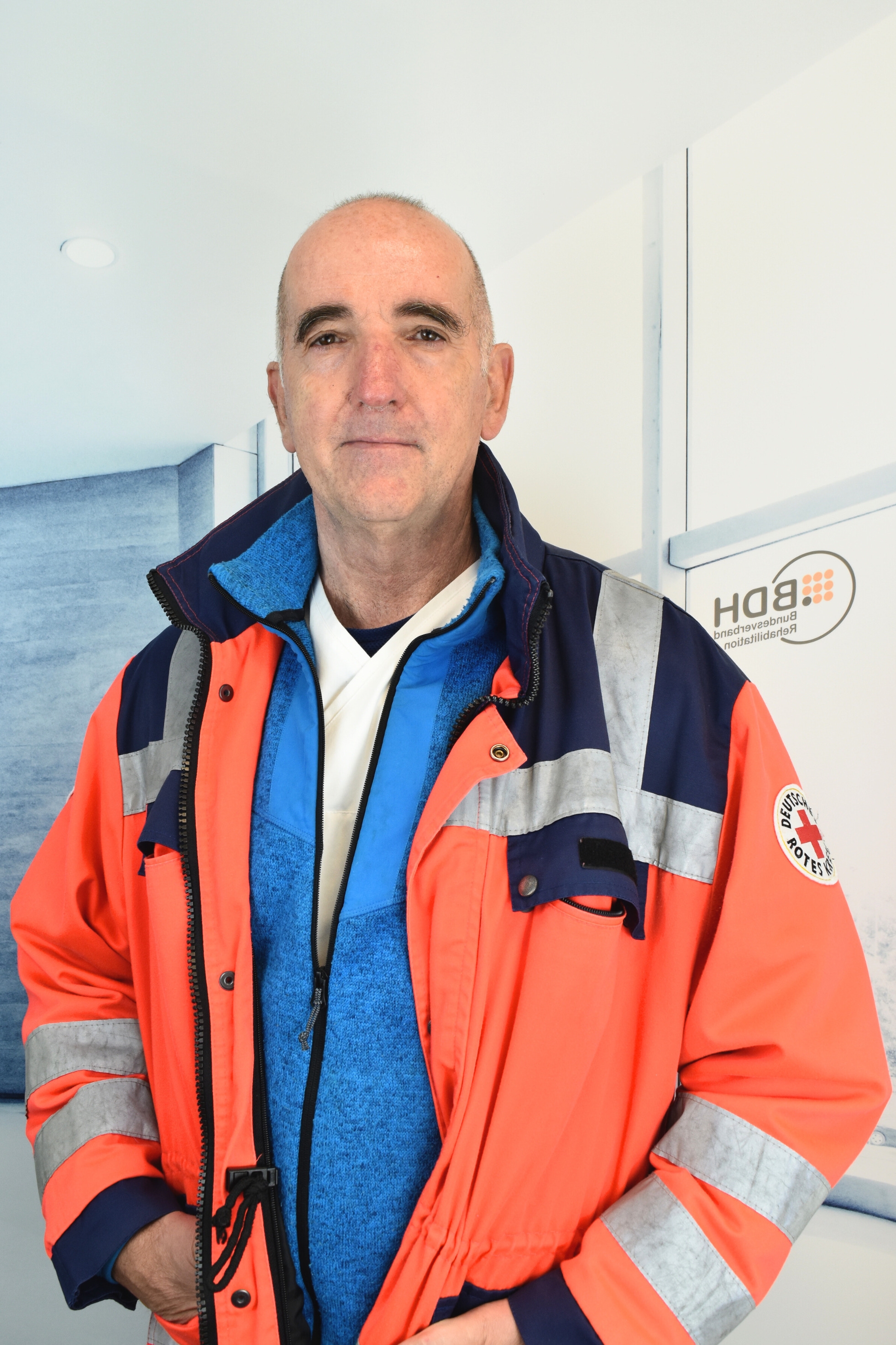 Kahlköpfiger großgewachsener Mann mit einer roten Warnjacke über seiner blauen Jacke