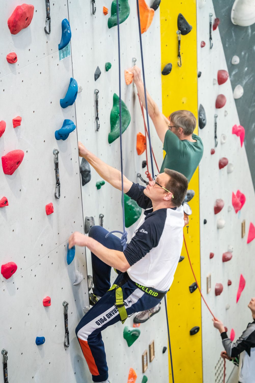Junger Mann klettert in einer Halle an einer  Kletterwand herauf