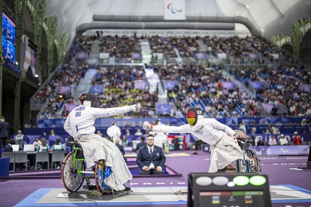 Zwei Fechter auf einem Podium. Im Hintergrund eine Tribüne mit vielen Zuschauern